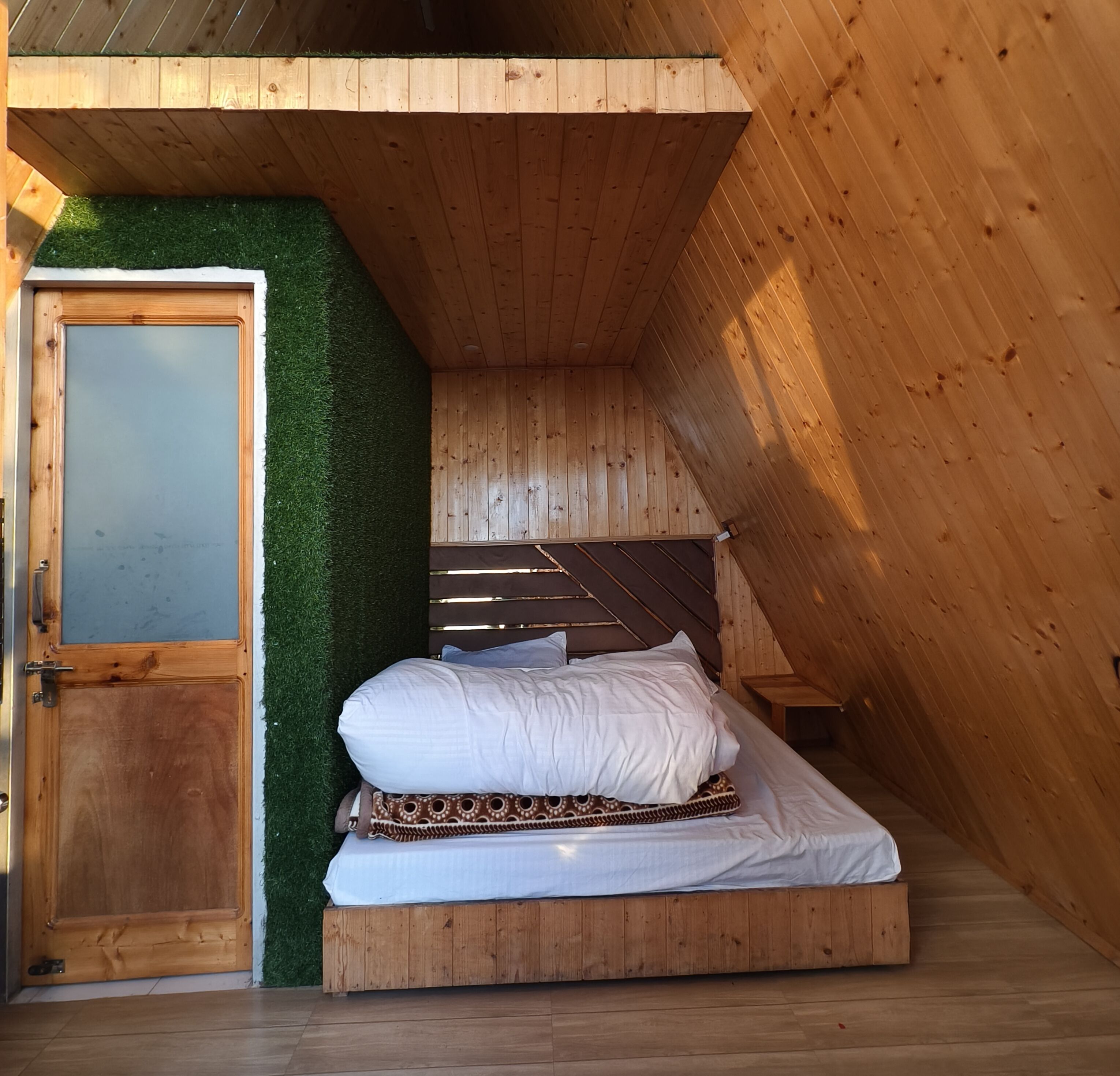 Um quarto pequeno estilo sótão, com madeira, uma cama, uma porta e uma parede com grama artificial.