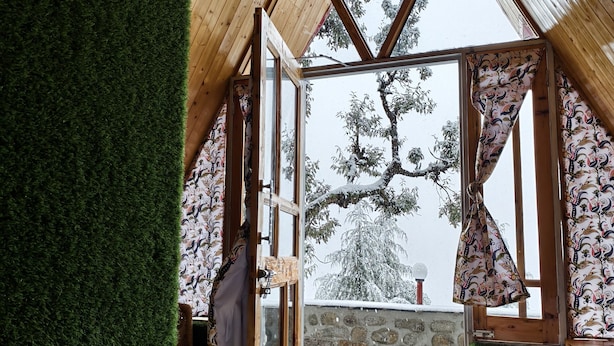 A cozy attic bedroom with a sloped wooden ceiling, a view of a snowy landscape, and a green artificial grass wall. - Eva Cabins (Dalhousie)
