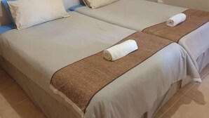 A hotel room with two beds, each with a beige blanket and a blue pillow. - Binga Rest Camp (Binga)