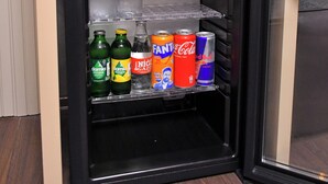 Un refrigerador pequeño negro con compartimento congelador, que contiene diversas bebidas y una botella de agua.