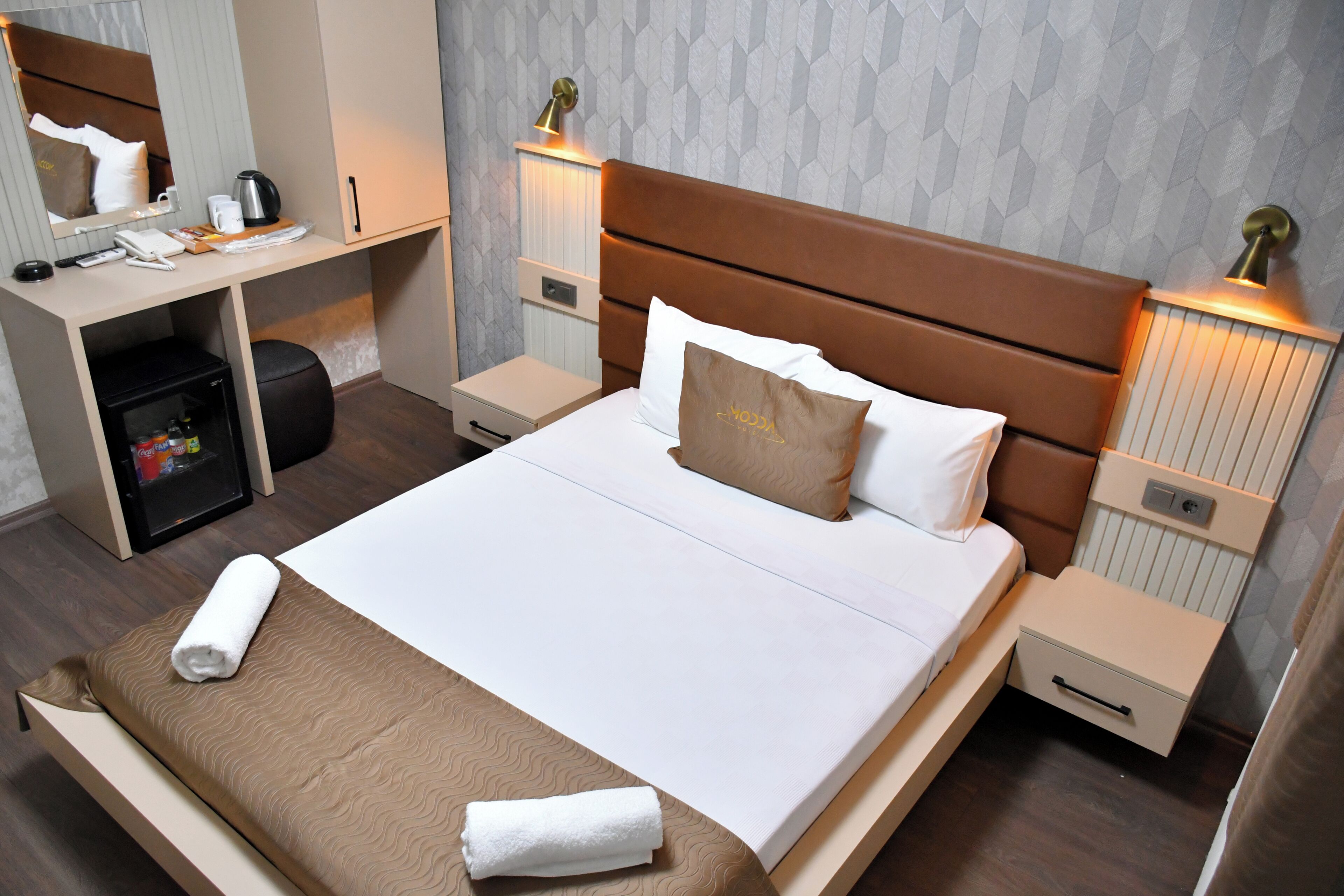 Una camera d'albergo ordinata con un letto grande, una scrivania con sedia, un piccolo armadio e lampade da comodino.