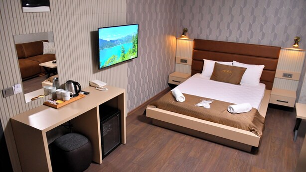 Una habitación de hotel con cama, mesitas de noche, escritorio, televisión y espejo.