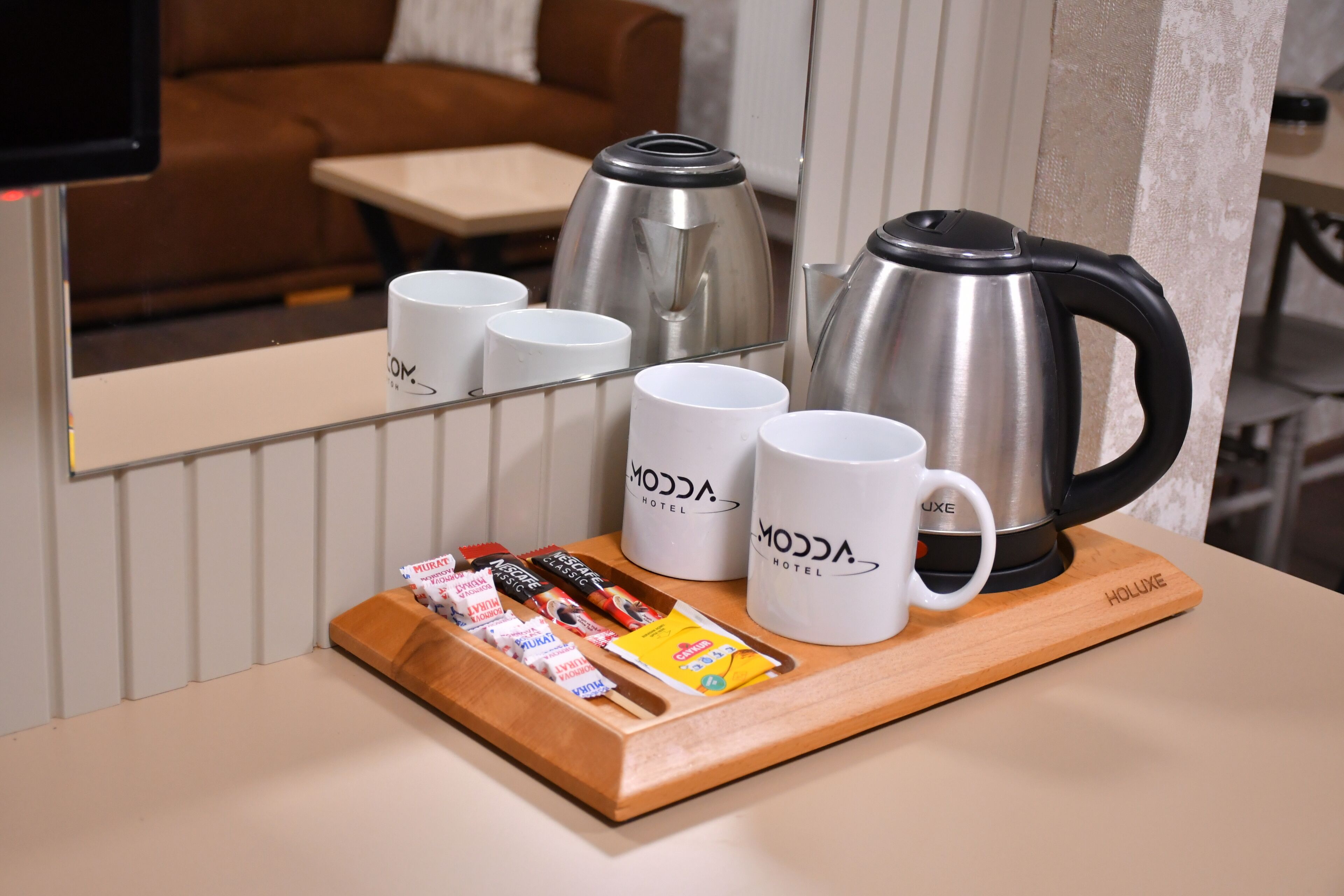 Une chambre d’hôtel avec un plateau en bois contenant des tasses, une bouilloire et une boîte de chocolats.