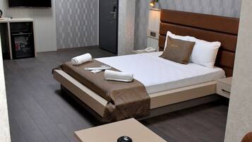 Habitación de hotel con cama, escritorio con televisor de pantalla plana, mesita de noche y dos sillones de cuero marrón.