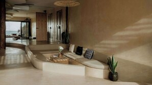 A modern living room with a curved sofa, a small round table, and a potted plant. - Villa Privada | Fully-Staffed Beachfront Getaway (Tulum)