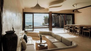 A modern living room with a large sofa, a dining table, and a view of the ocean. - Villa Privada | Fully-Staffed Beachfront Getaway (Tulum)