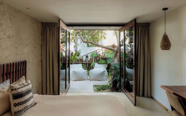 A bedroom with a large bed, a wooden headboard, a bedside table, and a view of a garden through a glass door. - Villa Privada | Fully-Staffed Beachfront Getaway (Tulum)