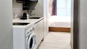 A modern hotel room with a kitchenette, a washing machine, a bed, and a bathroom. - Raviens TheBayment Nampo (Busan)