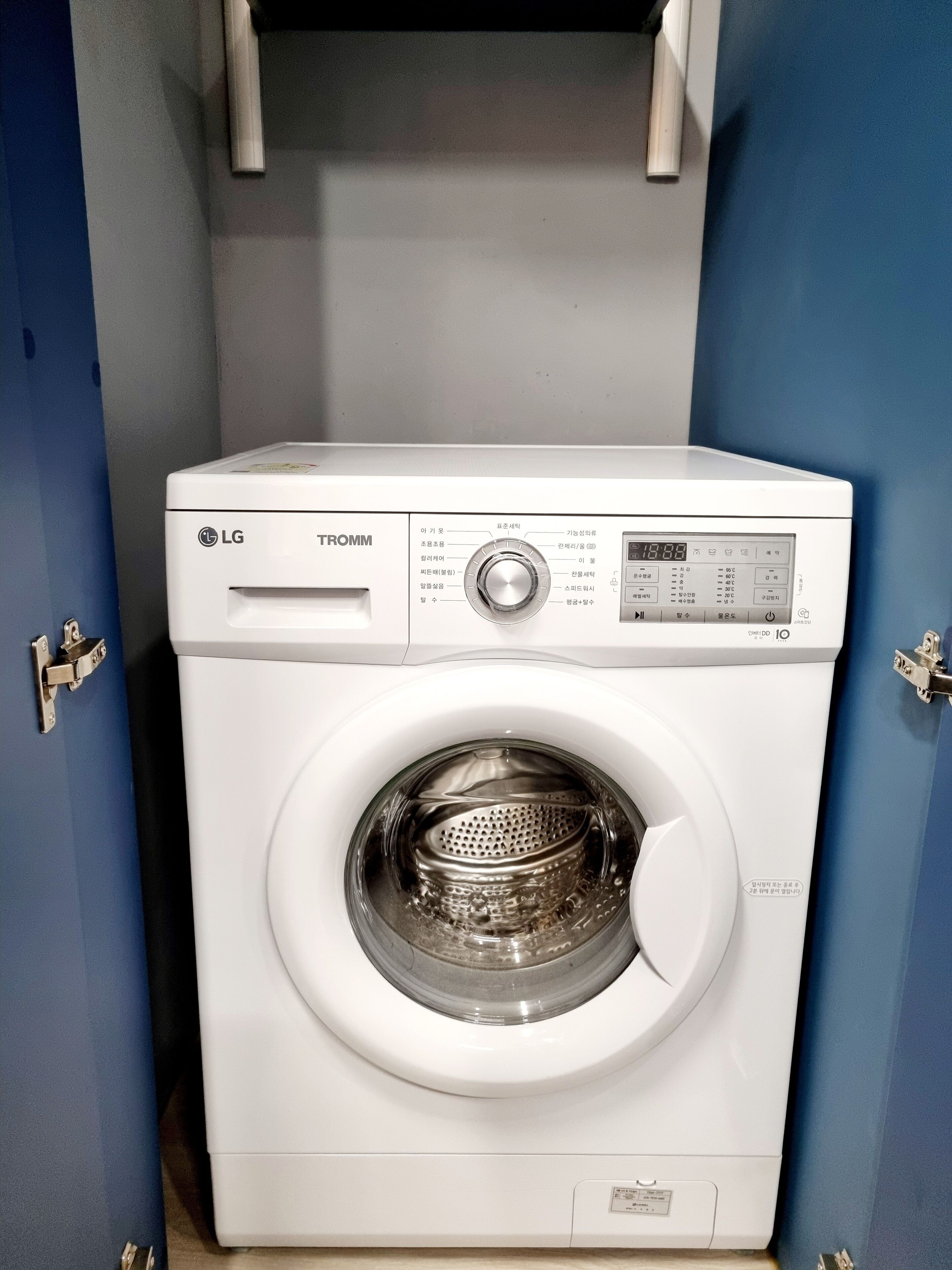 Un lave-linge LG TROMM à chargement frontal, installé dans une buanderie aux murs bleus et dotée d’une porte.