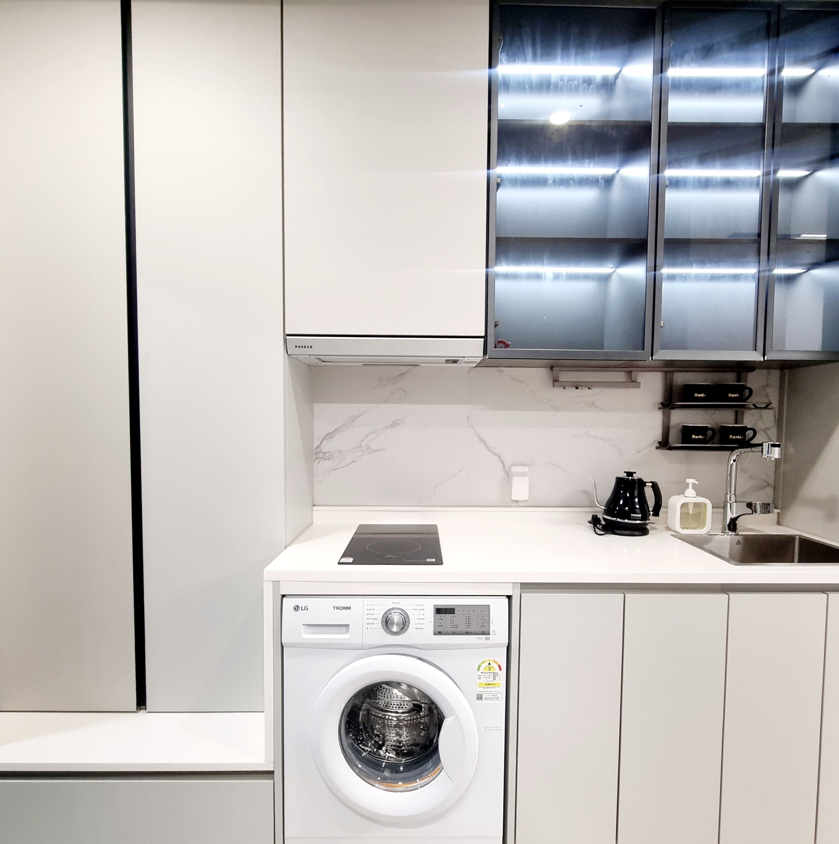 A compact kitchen with a built-in washer and dryer, stainless steel cabinets, a countertop with a coffee maker, and a sink.
