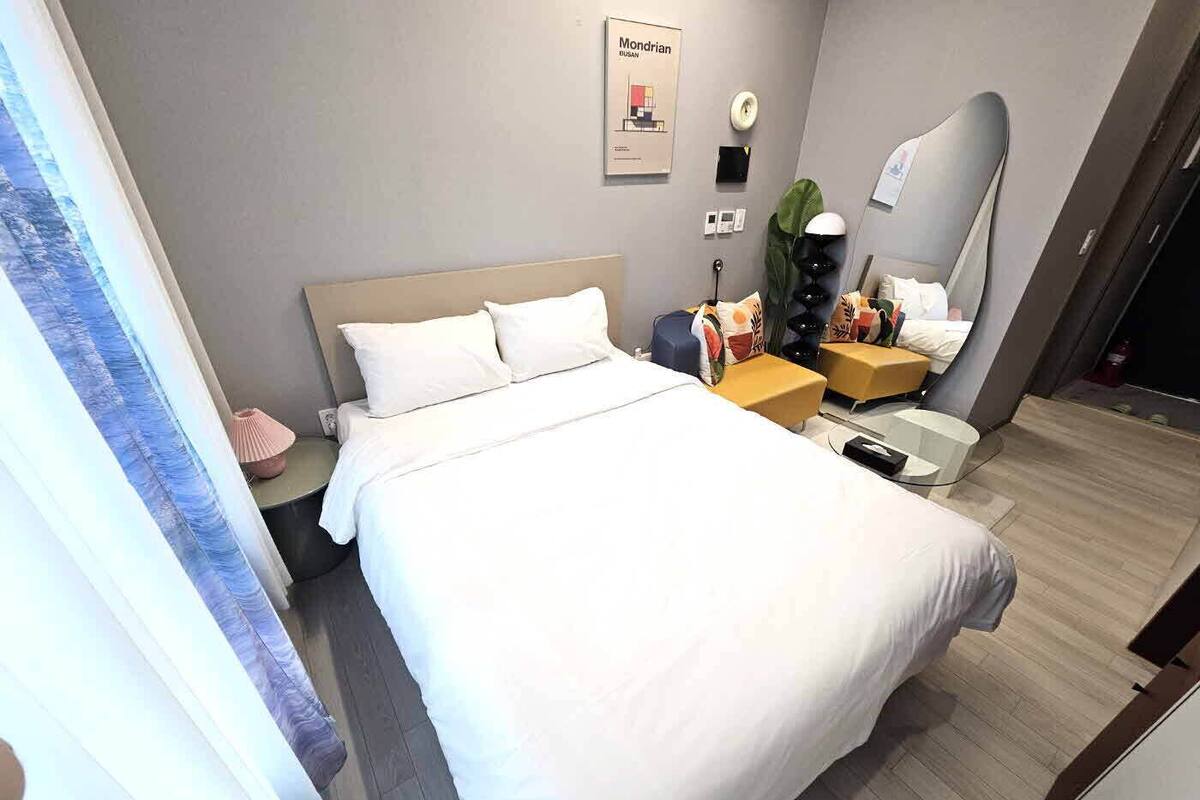 Una habitació d'hotel amb un llit gran, una taula de nit, una cadira, una taula petita, un mirall i un cartell a la paret.