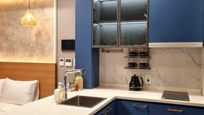 A modern kitchen with blue cabinets, a white countertop, a built-in microwave, and a coffee maker. - Raviens TheBayment Nampo (Busan)