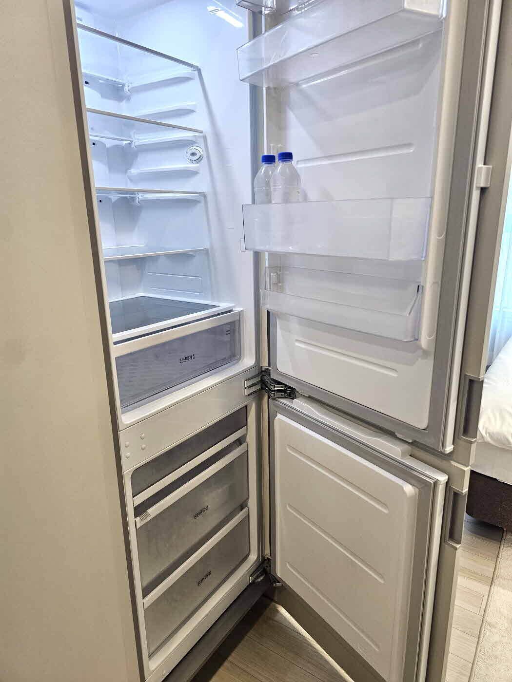 A compact refrigerator with multiple shelves and a freezer compartment, located in a corner of a room with a tiled floor.