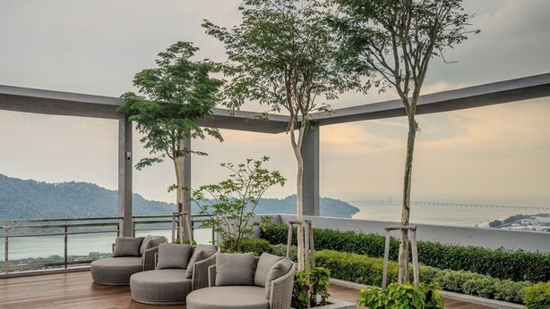 A modern outdoor seating area with a wooden deck, grey cushioned chairs, and potted plants. - Iconic Regency Service Residences - Managed by Iconic Hotel (George Town)