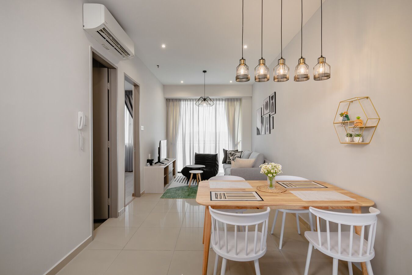 A modern living room with a dining area, featuring a wooden table, white chairs, and pendant lighting.