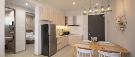 Una cocina moderna con refrigerador, microondas y armarios de madera. Se observa una mesa de comedor con sillas y un florero con flores.