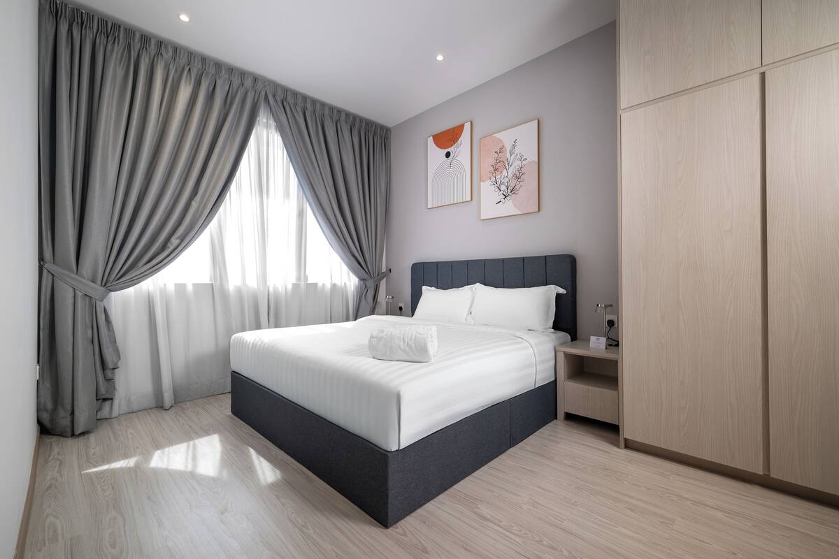 A modern bedroom with a large bed, grey curtains, and wooden flooring.