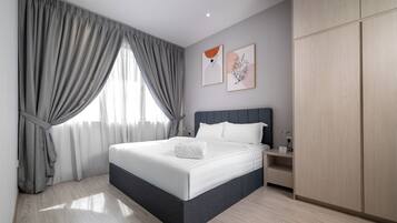A modern bedroom with a large bed, grey curtains, and wooden flooring.