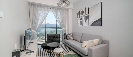 Ein modernes Wohnzimmer mit einem grauen Sofa, einem schwarzen Sessel, einem runden Tisch und Blick auf eine Stadt durch große Fenster.