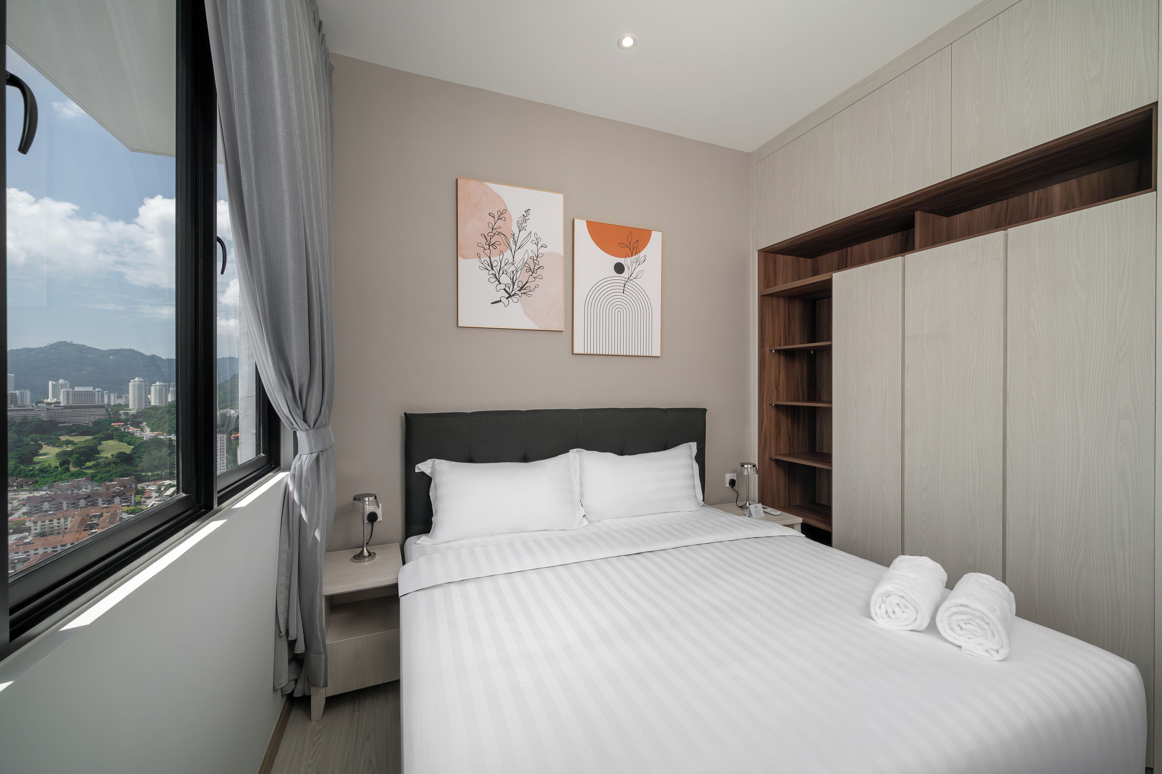Une chambre d’hôtel moderne avec un grand lit, une table de chevet, une petite table de nuit avec un verre à vin, une armoire et deux œuvres d’art encadrées accrochées au mur.