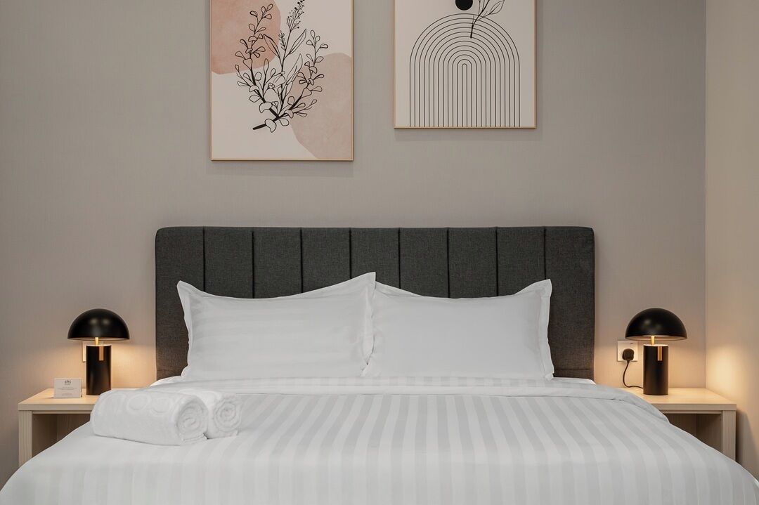 A neatly made bed with white linens and pillows, flanked by two bedside tables with lamps. Above the bed, there are two framed artworks on the wall.