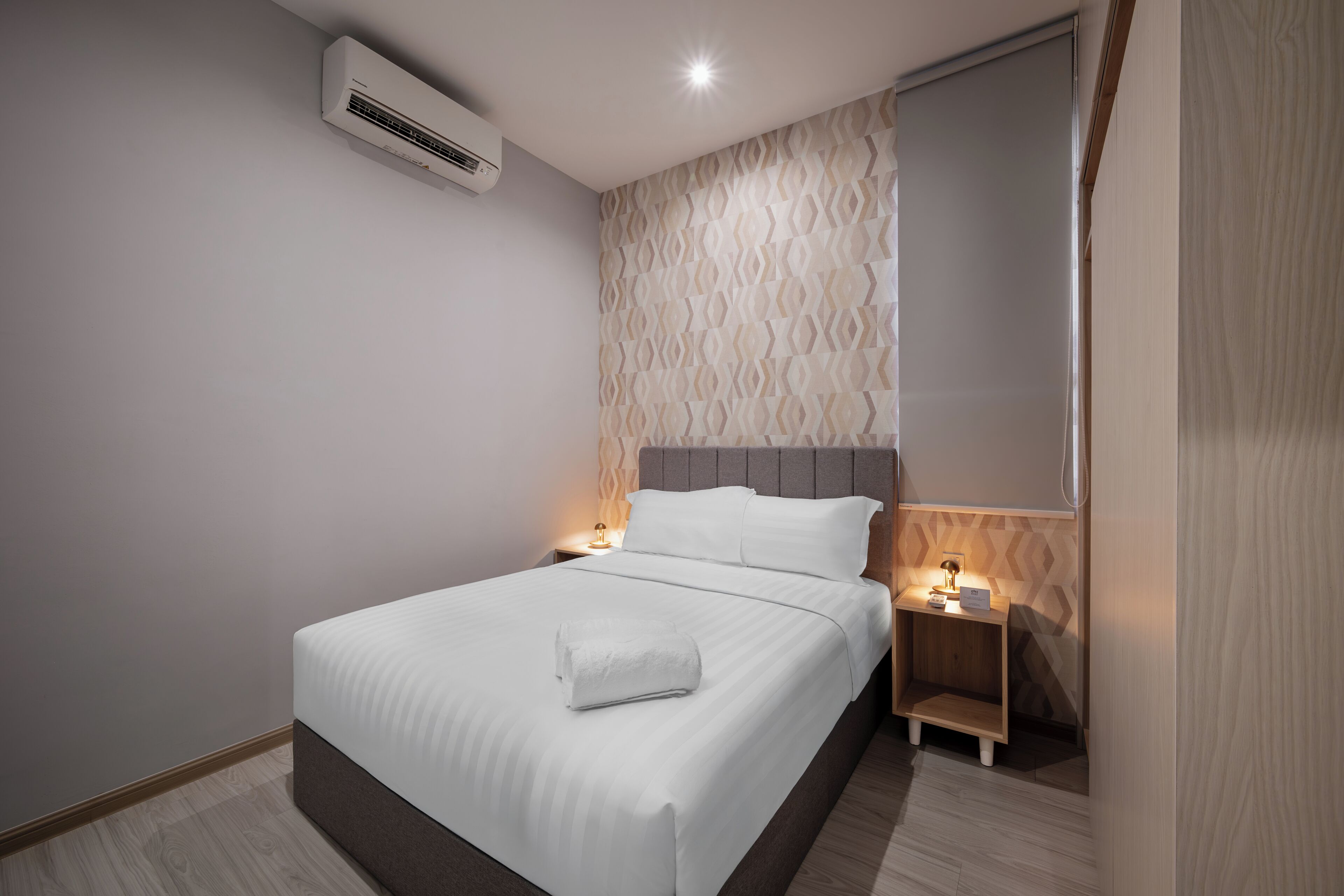 Una habitación de hotel moderna con una cama bien hecha, una mesita de noche con lámpara y un aire acondicionado instalado en la pared.