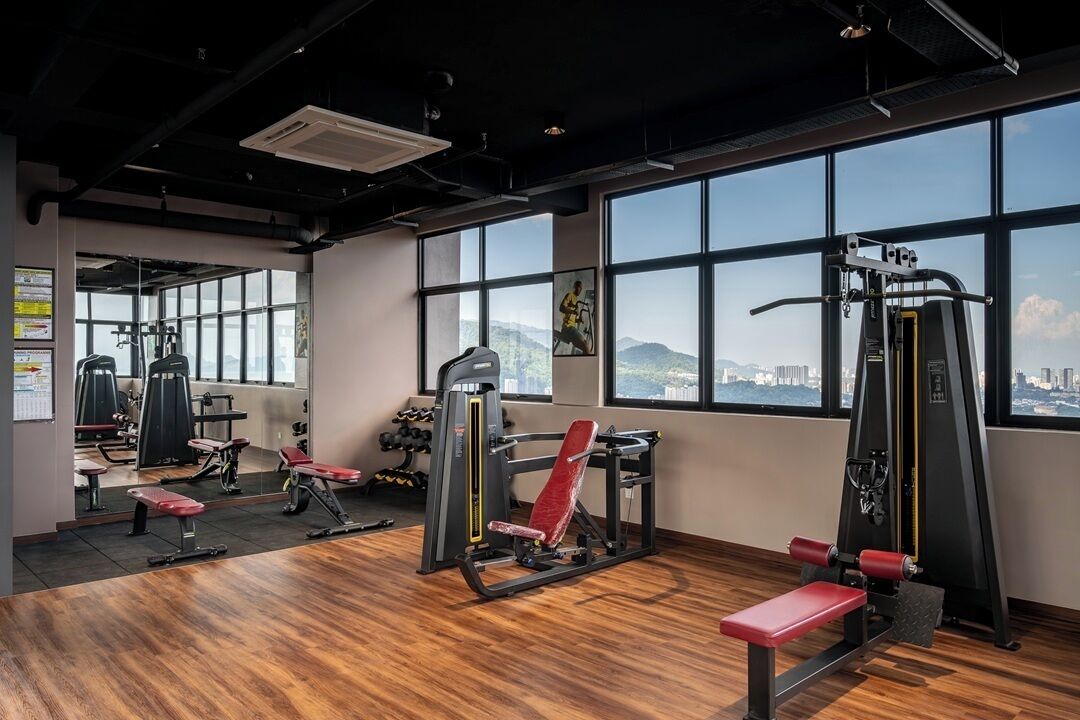 Un gimnasio con equipamiento de ejercicio, ventanas amplias y vista a la ciudad.