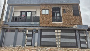 A two-story building with a balcony on the upper floor, a stone facade on the right side, and a grey exterior on the left. - COSY apartment in Abidjan (Abidjan)