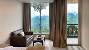 Une chambre d’hôtel avec un lit, un canapé, une petite table et une vue sur les montagnes, visible à travers de grandes fenêtres.