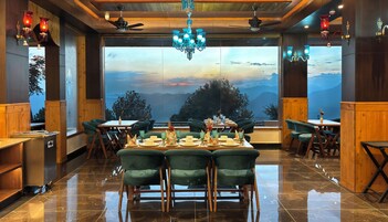 A restaurant with a view of mountains, wooden paneling, green upholstered chairs, and a chandelier.