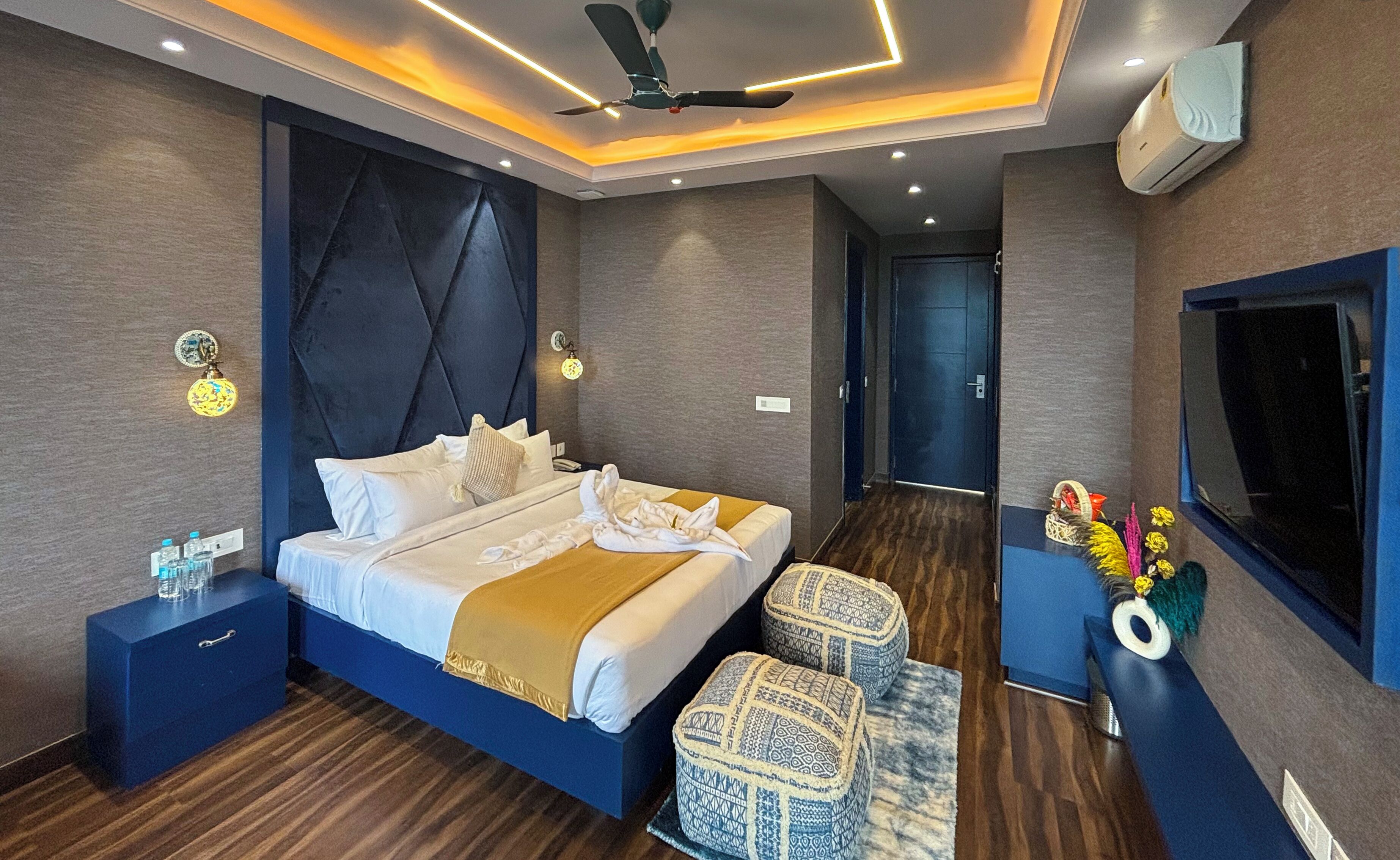 A modern hotel room with a large bed, a ceiling fan, a flat-screen TV, and a small side table with a vase of flowers.