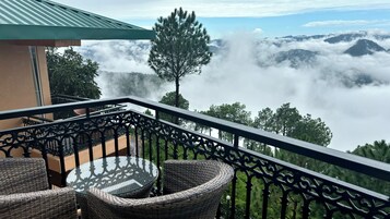 Un balcón con mobiliario de mimbre y vistas a montañas y nubes.