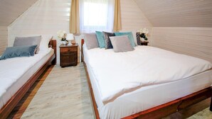 A bedroom with two beds, wooden flooring, a window with curtains, and a nightstand with a lamp and flowers. - Stunning home in Mielenko with WiFi (Mielenko)