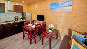 A wooden interior with a dining table set for four, a kitchen with a stove and refrigerator, and a painting of a beach on the wall. - Stunning home in Mielenko with WiFi (Mielenko)