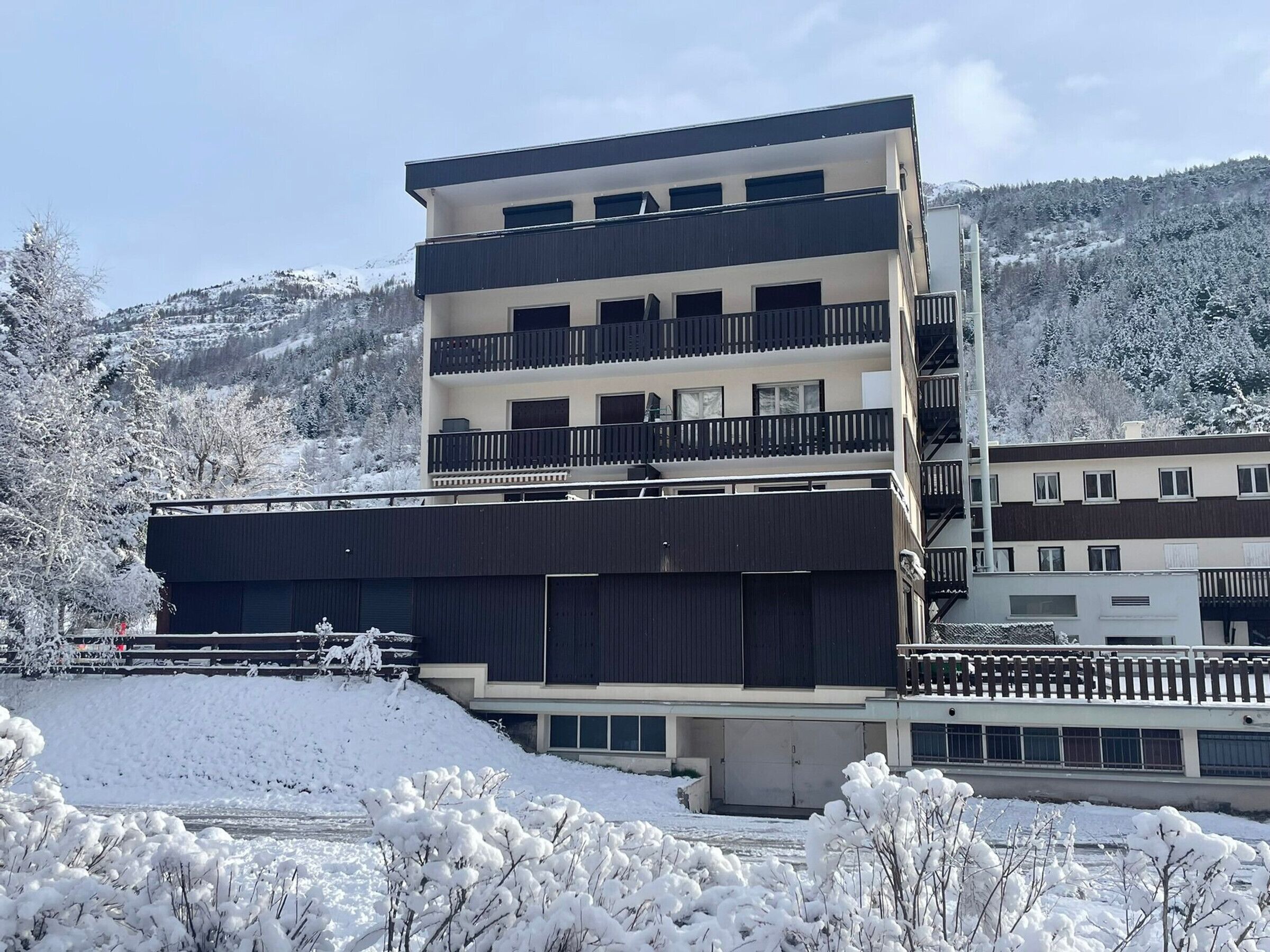 Un edificio de varios pisos con balcones, techo plano y un paisaje cubierto de nieve.