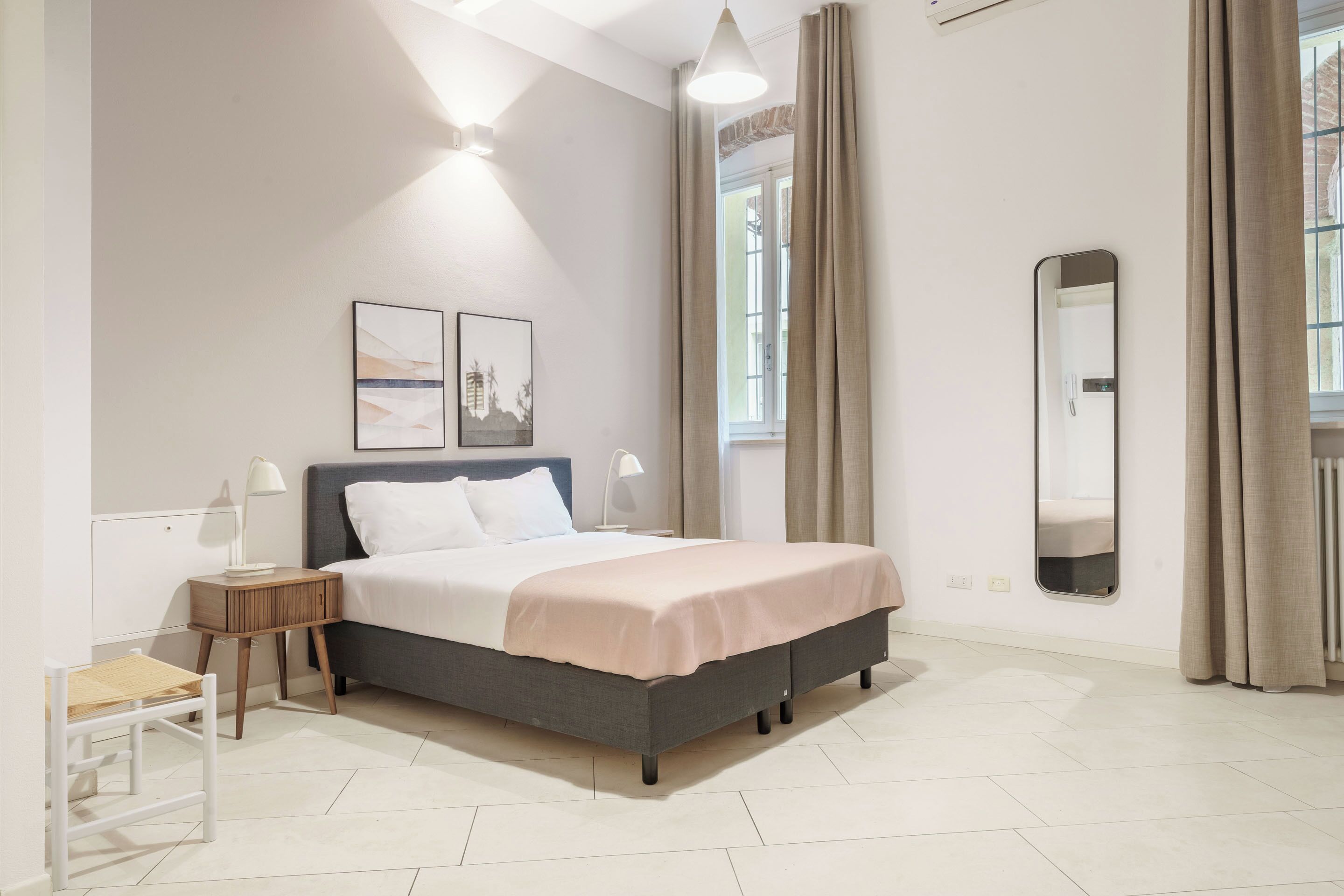 A modern bedroom with a bed, bedside tables, a chair, a mirror, and artwork on the wall.