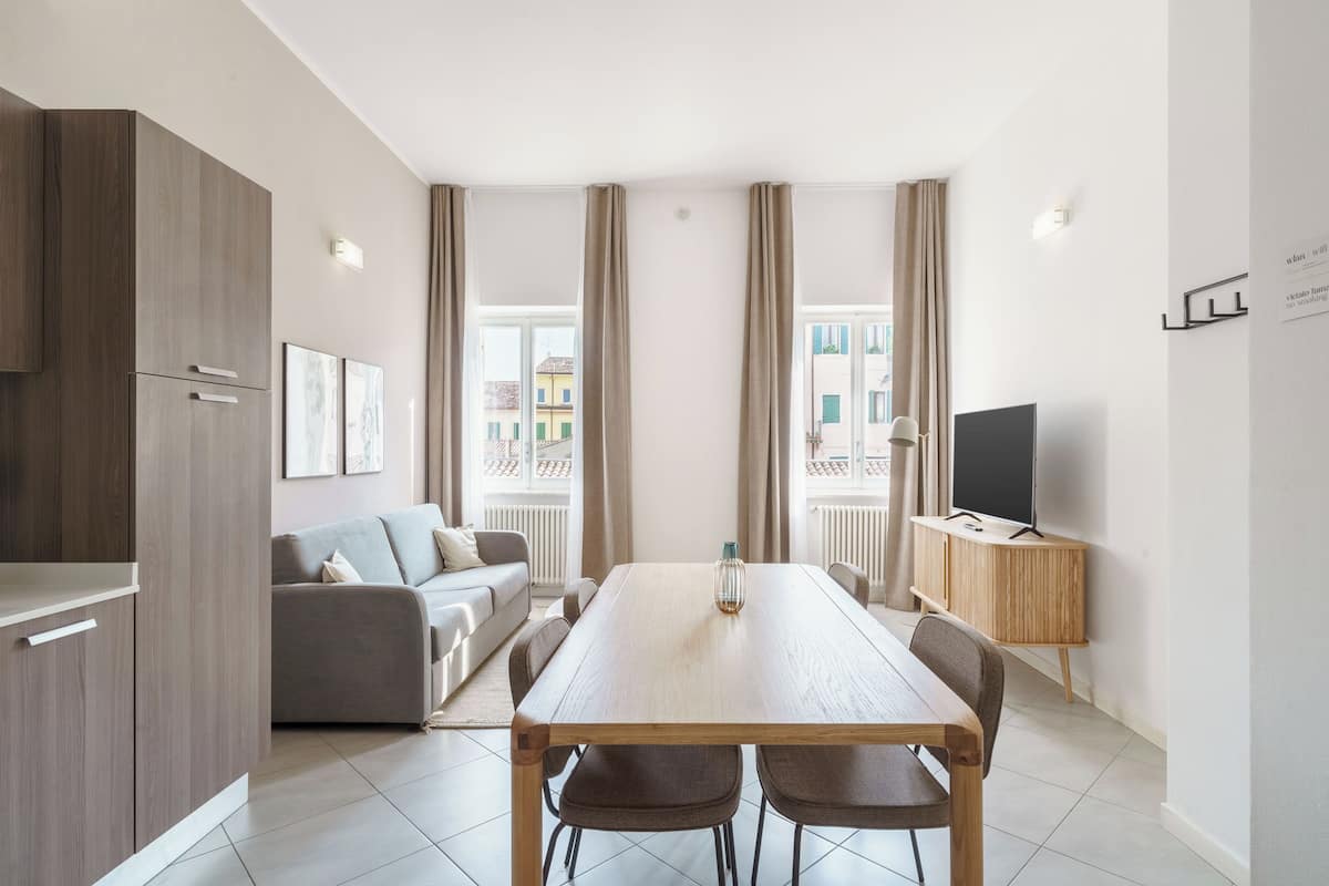 Ein modernes Wohnzimmer mit Esstisch, Sofa, Fernseher und großen Fenstern.