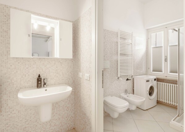 A modern bathroom with a white sink, a mirror, a toilet, a bidet, and a washing machine. - Limehome Verona La Vigna in Città (Verona)