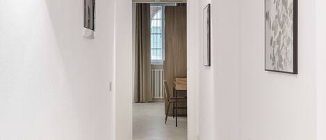 A hallway with white walls, a tiled floor, and a dining area in the background.