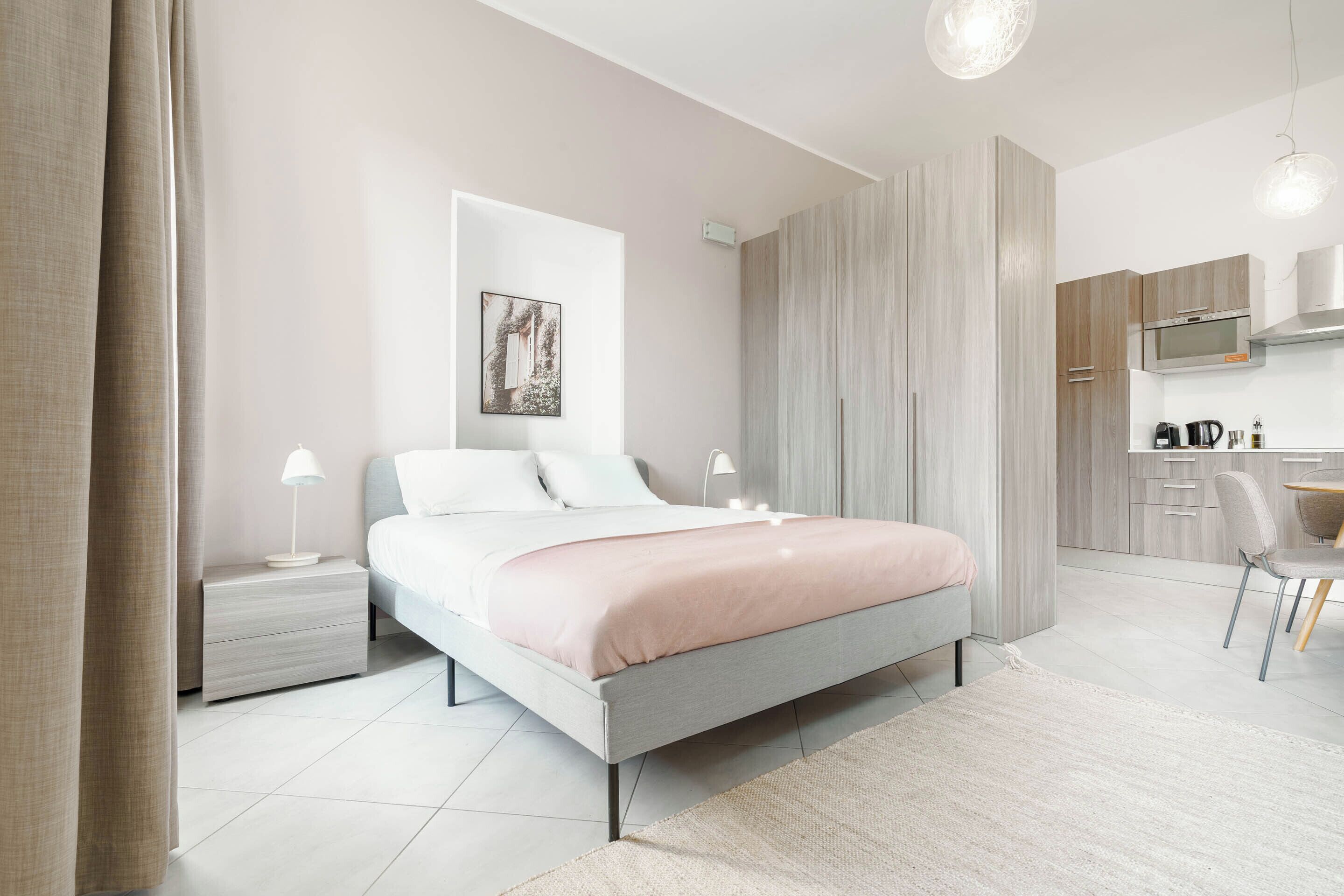 Une chambre moderne comprenant un lit, des tables de chevet, un bureau et un coin cuisine.