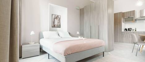 Une chambre moderne comprenant un lit, des tables de chevet, un bureau et un coin cuisine.