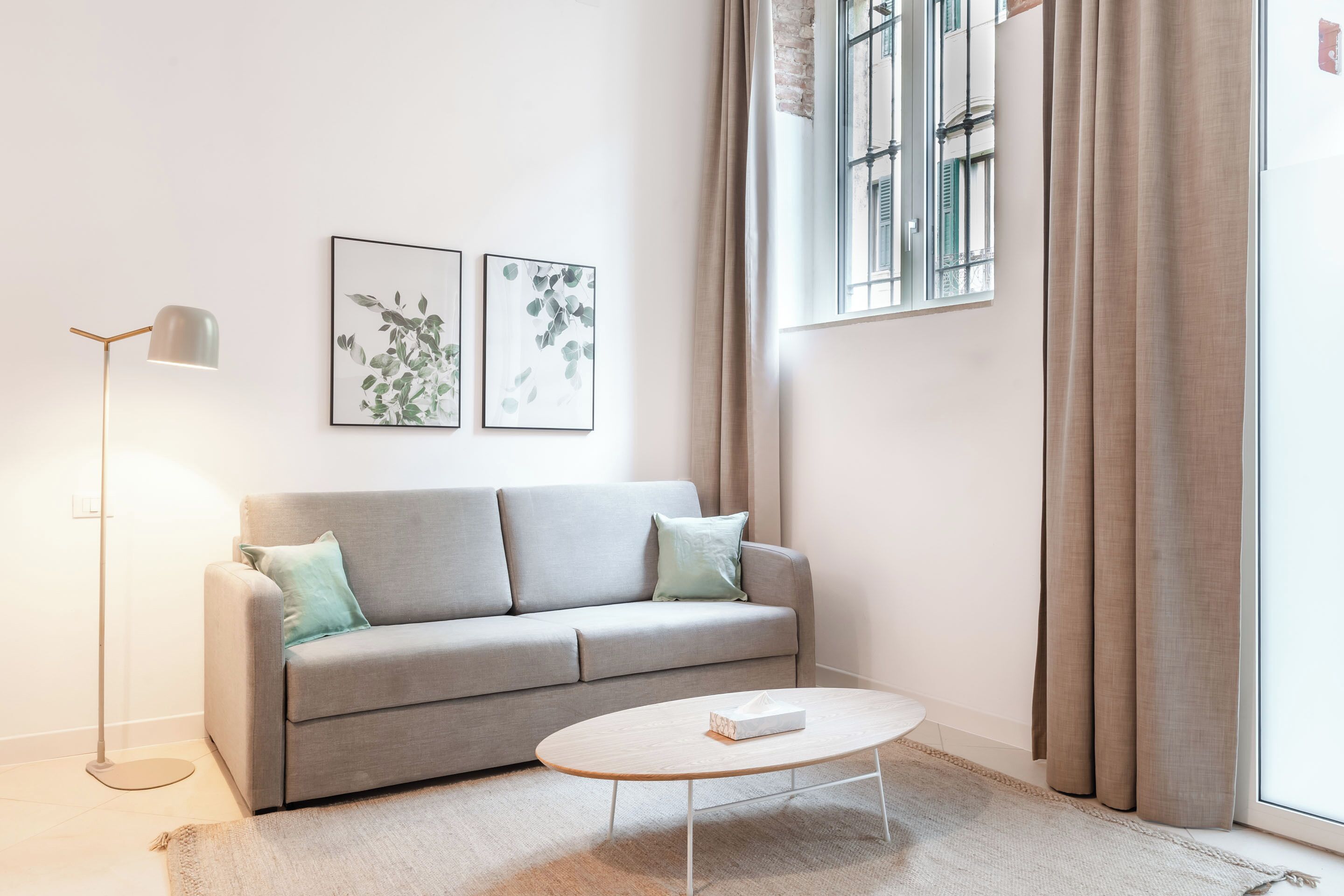 A modern living room with a grey sofa, a floor lamp, and two framed artworks on the wall.