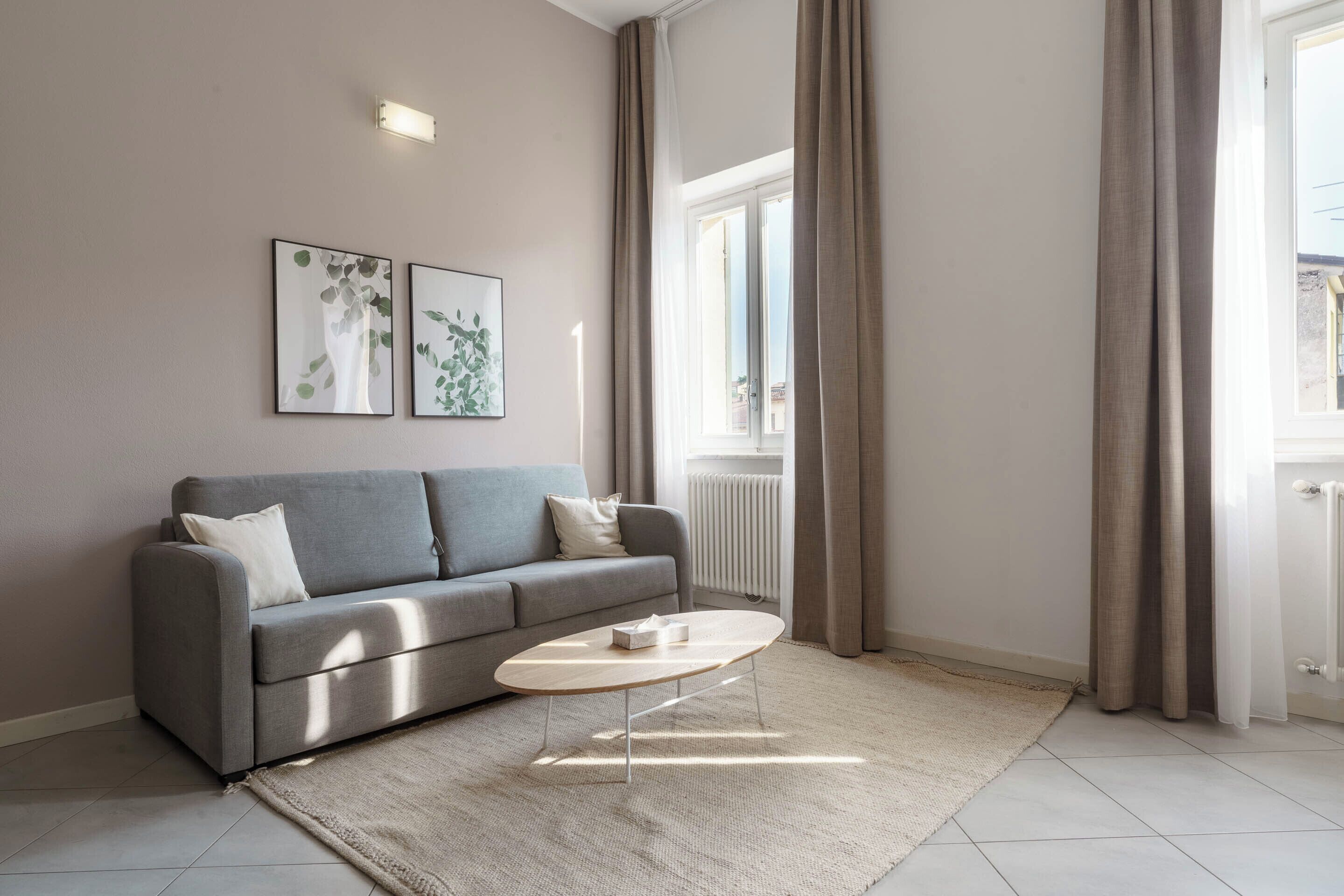 Un salon moderne avec un canapé gris, une table basse en bois et deux œuvres d’art encadrées accrochées au mur.