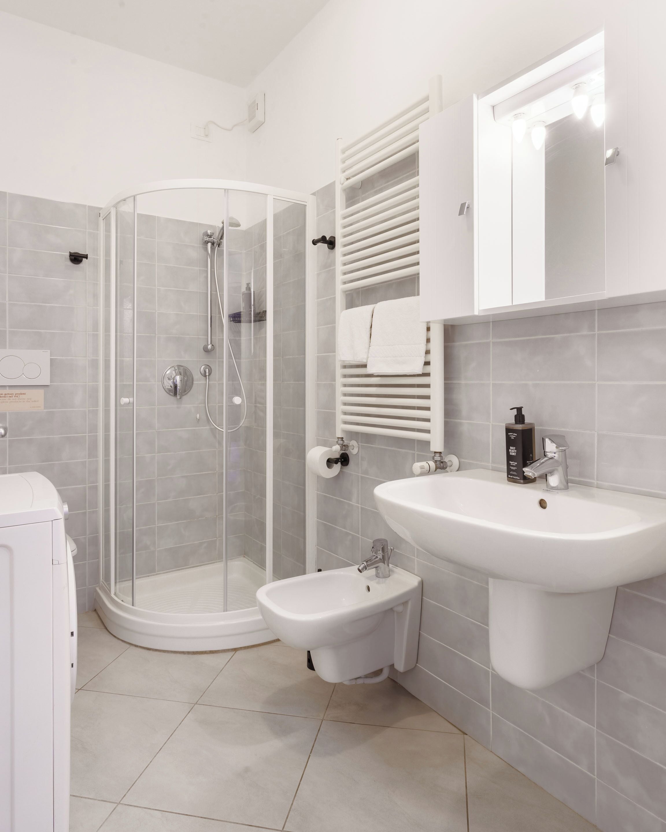 Un baño moderno con ducha de vidrio, lavamanos pedestal y un pequeño bidé.