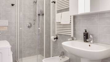 Un baño moderno con ducha de vidrio, lavamanos pedestal y un pequeño bidé.