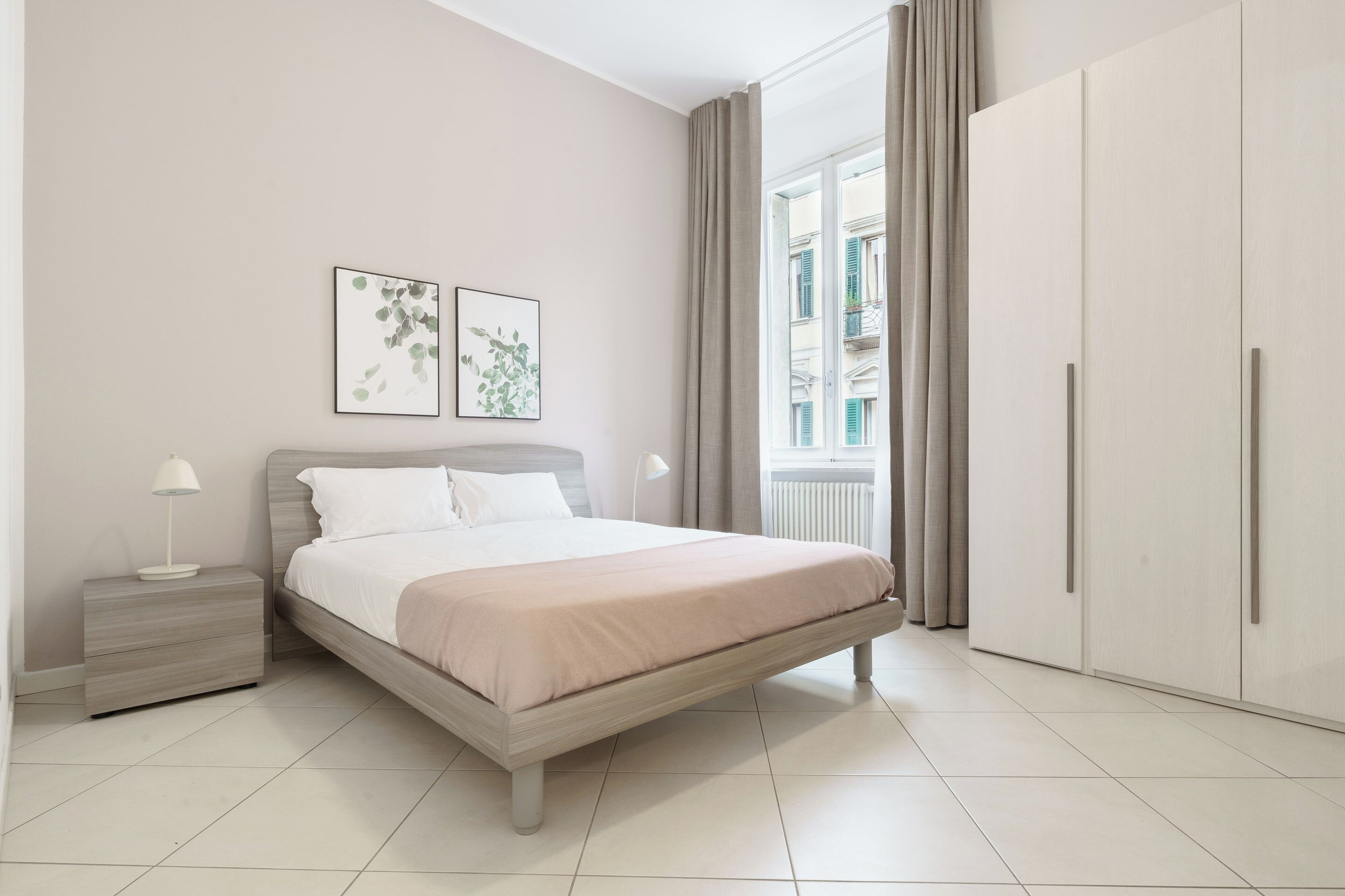 Ein Schlafzimmer mit Bett, Nachttischen, einem Kleiderschrank und einem Fenster mit Vorhängen.