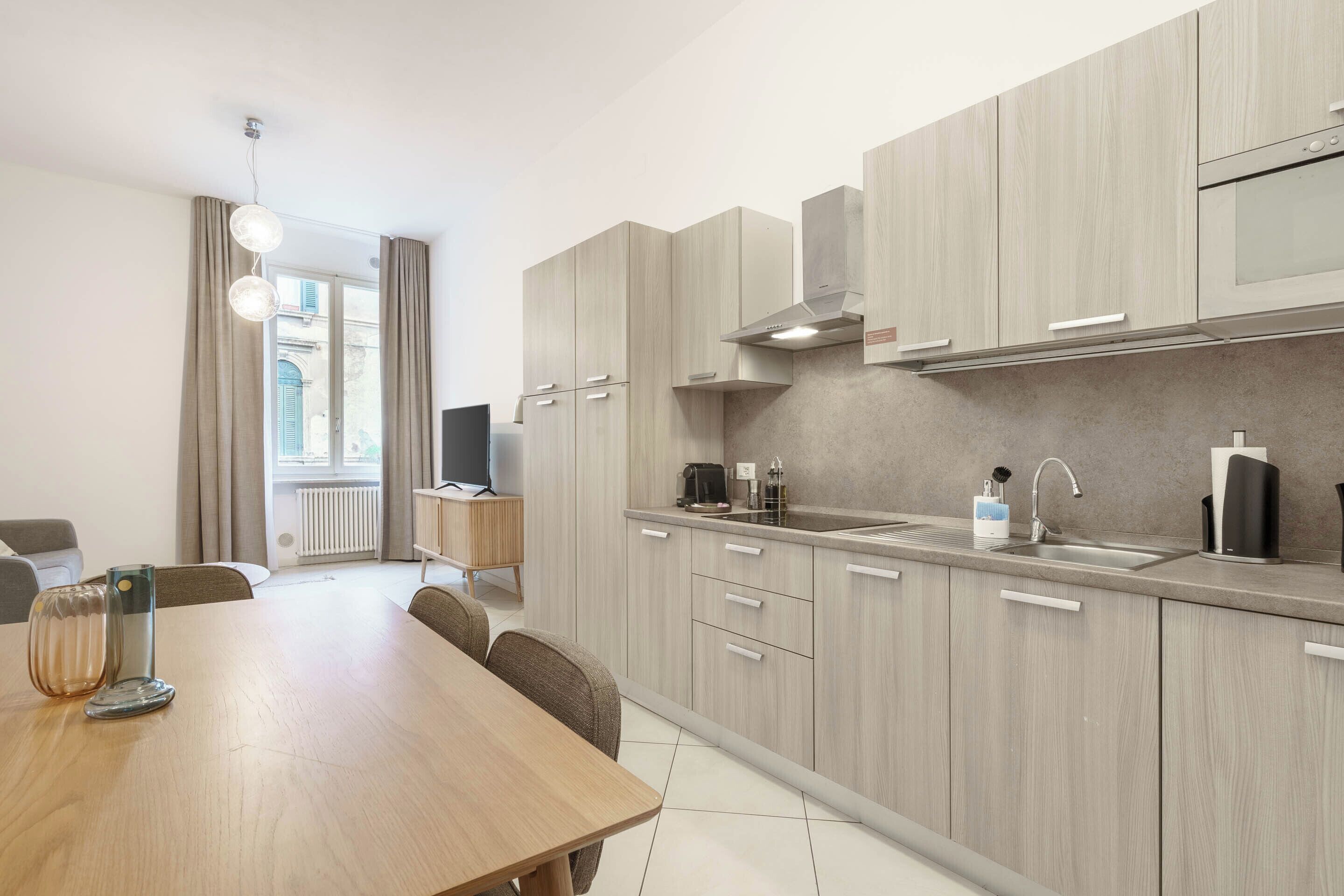 Een moderne keuken met lichte houten kastjes, een RVS-spoelbak en een eethoek met een houten tafel en stoelen.