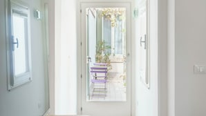 Un pasillo con una puerta blanca que da a un espacio exterior con un banco y una planta en maceta.