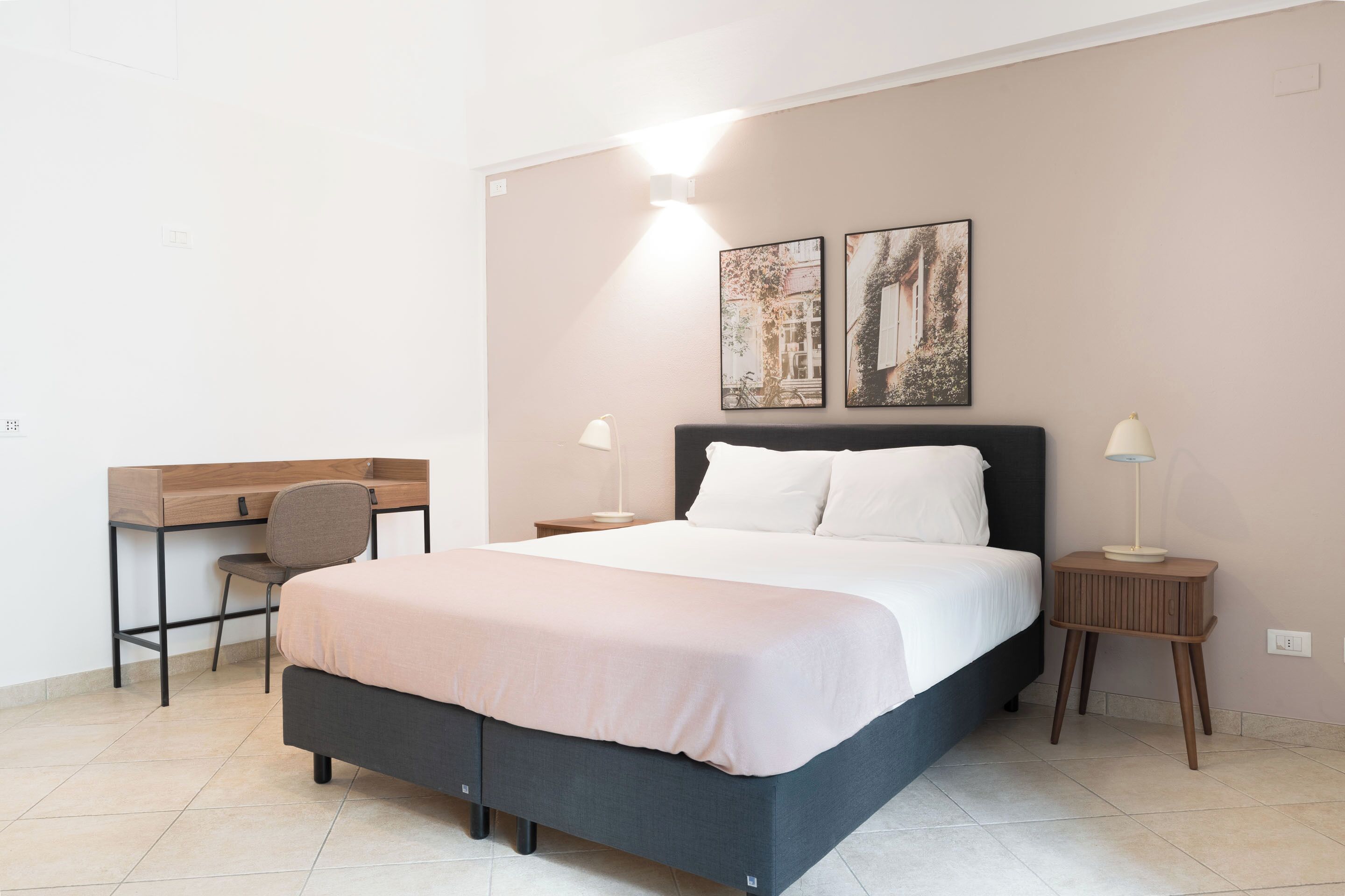 A bedroom with a bed, a desk, two bedside tables, and two wall-mounted lamps.