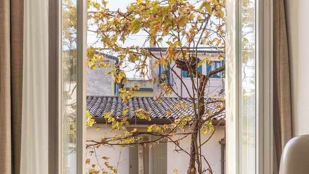 Una ventana con vista a un edificio de techo con tejas y un árbol de hojas amarillas.